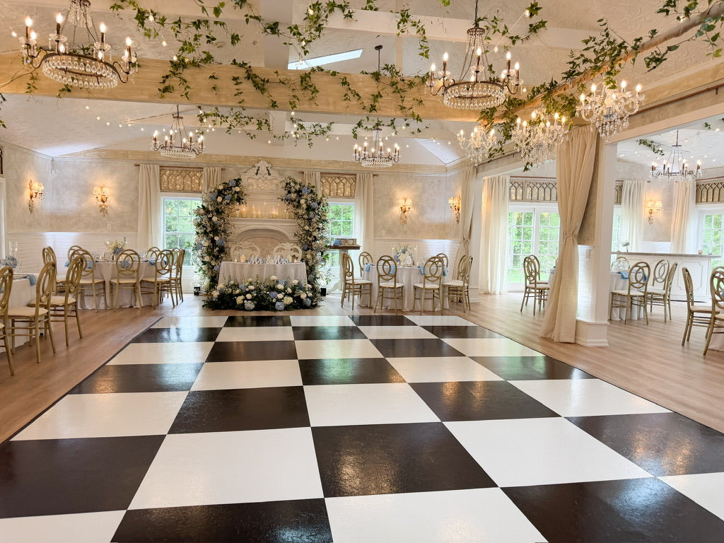 Decorative indoor setting with chandeliers, floral arrangements, and a checkered floor.